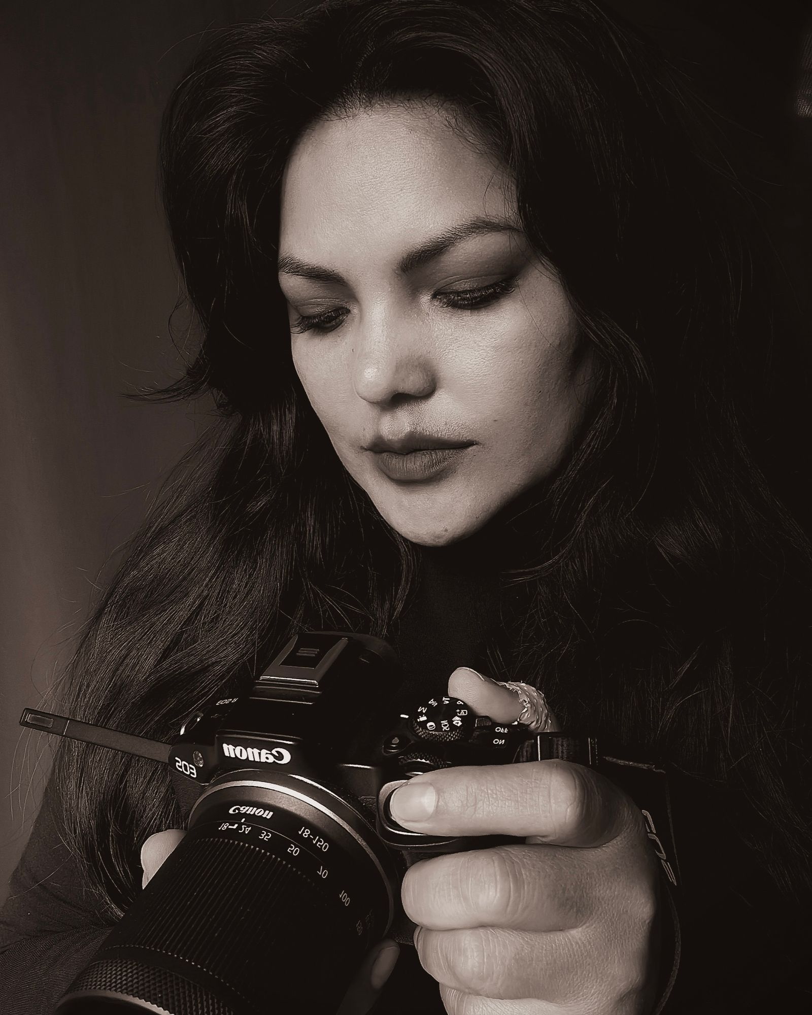 Black and white portrait of a photographer looking down at her camera.